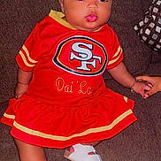Dlonni is registered to the contest to win money with this photo: baby, child, infant, portrait, sitting, couch, red_outfit, football_jersey, sportswear, san_francisco_49ers, headband, bow, sandals, bracelet, smiling, wide_eyed, indoor, furniture, fashion, football_fan