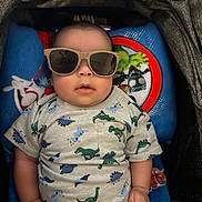 Mateo joined the competition — help win amazing prizes! baby, child, infant, sunglasses, dinosaur_clothing, stroller, seated, portrait, face, hands, short_sleeves, pajamas, blue_blanket, colorful, indoor, cute, serious_expression, cozy, photography, fashion