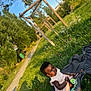 child, toddler, grass, outdoor, blanket, dress, socks, pathway, wooden_structure, sunlight, greenery, nature, playground, person, summer, daylight, park, cute, young_child, sitting