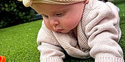 Mabel-Lilly is registered to the contest to win money with this photo: baby, headband, flower, toy, green_grass, outdoor, knit_sweater, crawling, child, person, curious, colorful, soft_light, background_blur, adult, sitting, playful, closeup, nature, cute