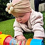 baby, headband, flower, toy, green_grass, outdoor, knit_sweater, crawling, child, person, curious, colorful, soft_light, background_blur, adult, sitting, playful, closeup, nature, cute
