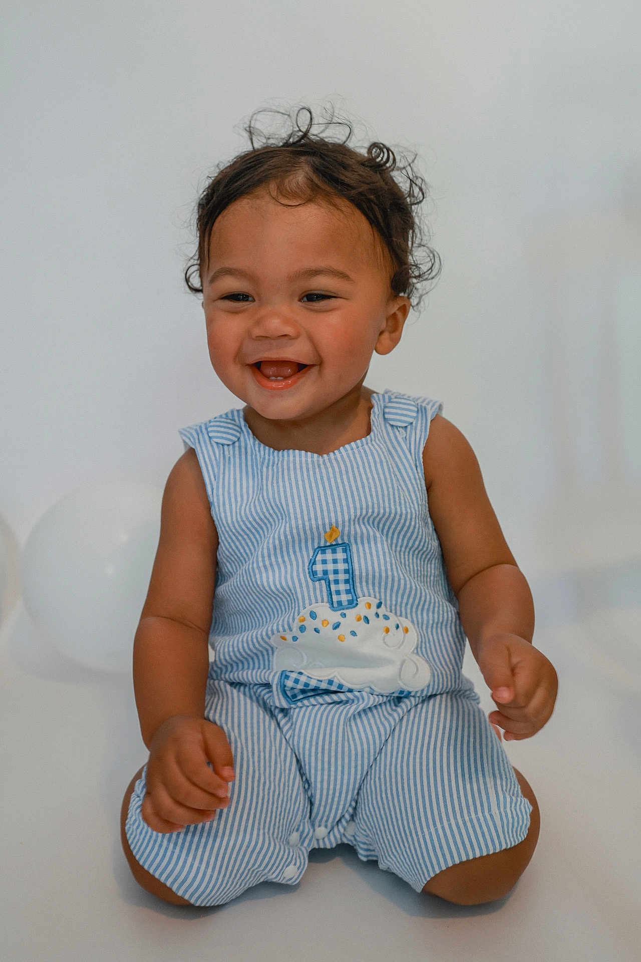 Caden joined the competition — help win amazing prizes! toddler, child, smiling, happy, curly_hair, striped_clothing, blue_outfit, birthday_cake, celebration, balloons, sitting, cute, one_year_old, portrait, indoors, baby, joyful, candle, festive, playful