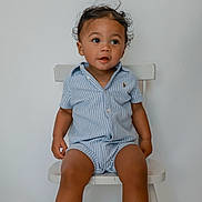 Caden joined the competition — help win amazing prizes! toddler, child, curly_hair, blue_romper, striped_clothing, white_chair, indoor, toy_blocks, playful, sitting, cute, young_child, expression, legs, minimalist, colorful, wooden_chair, looking_away, casual, happy