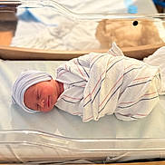 Isabella is registered to the contest to win money with this photo: newborn, baby, swaddled, hospital, blanket, bassinet, sleeping, infant, cap, bed, peaceful, soft_lighting, resting, cute, person, portrait, healthcare, nursery, newborn_hat, wrapped