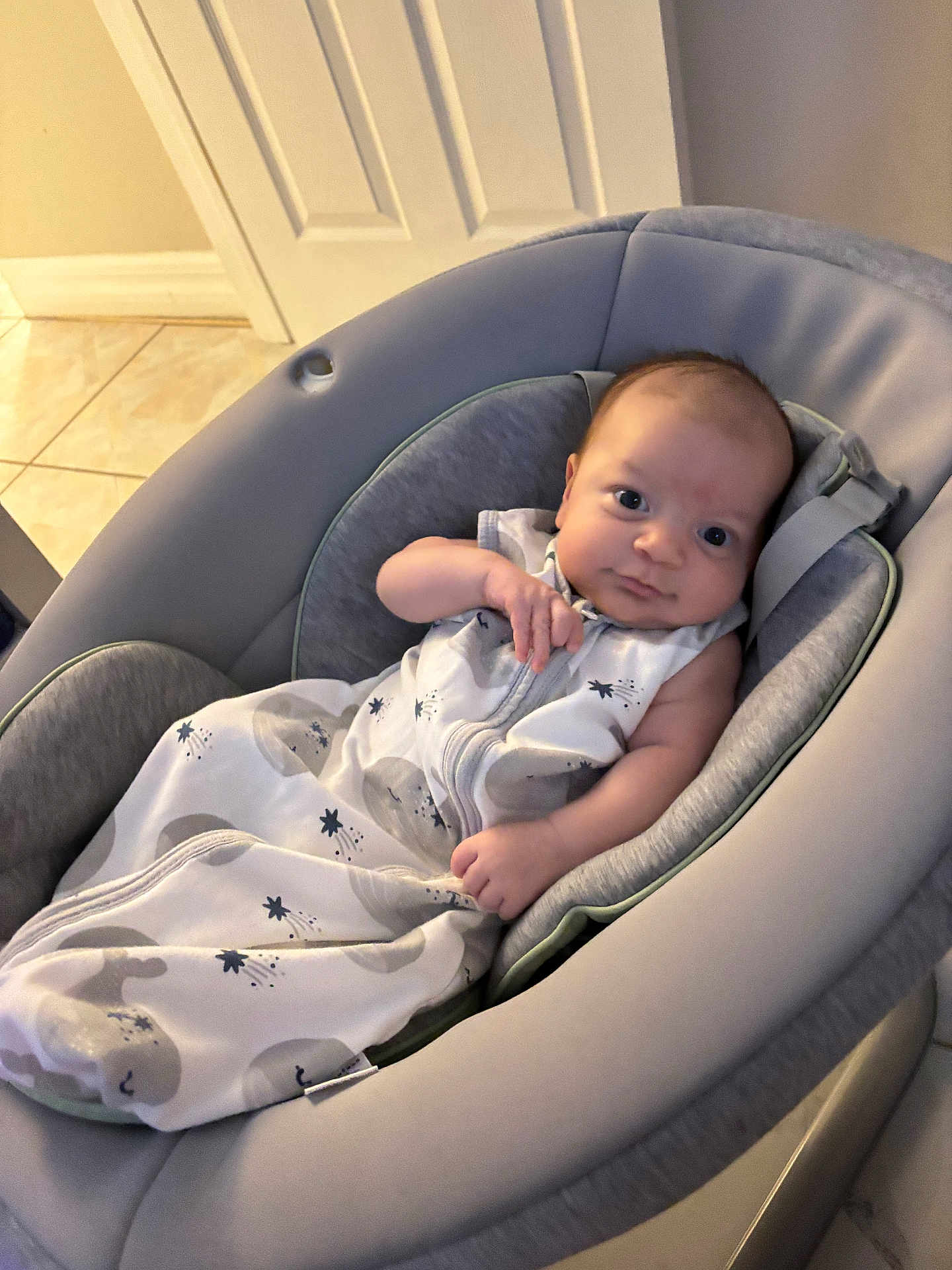 Emmanuel is registered to the contest to win money with this photo: baby, infant, baby_seat, sleep_sack, clothing, indoor, floor_tile, door, face, person, child, cute, gaze, relaxing, cozy, home, comfort, newborn, expression, soft