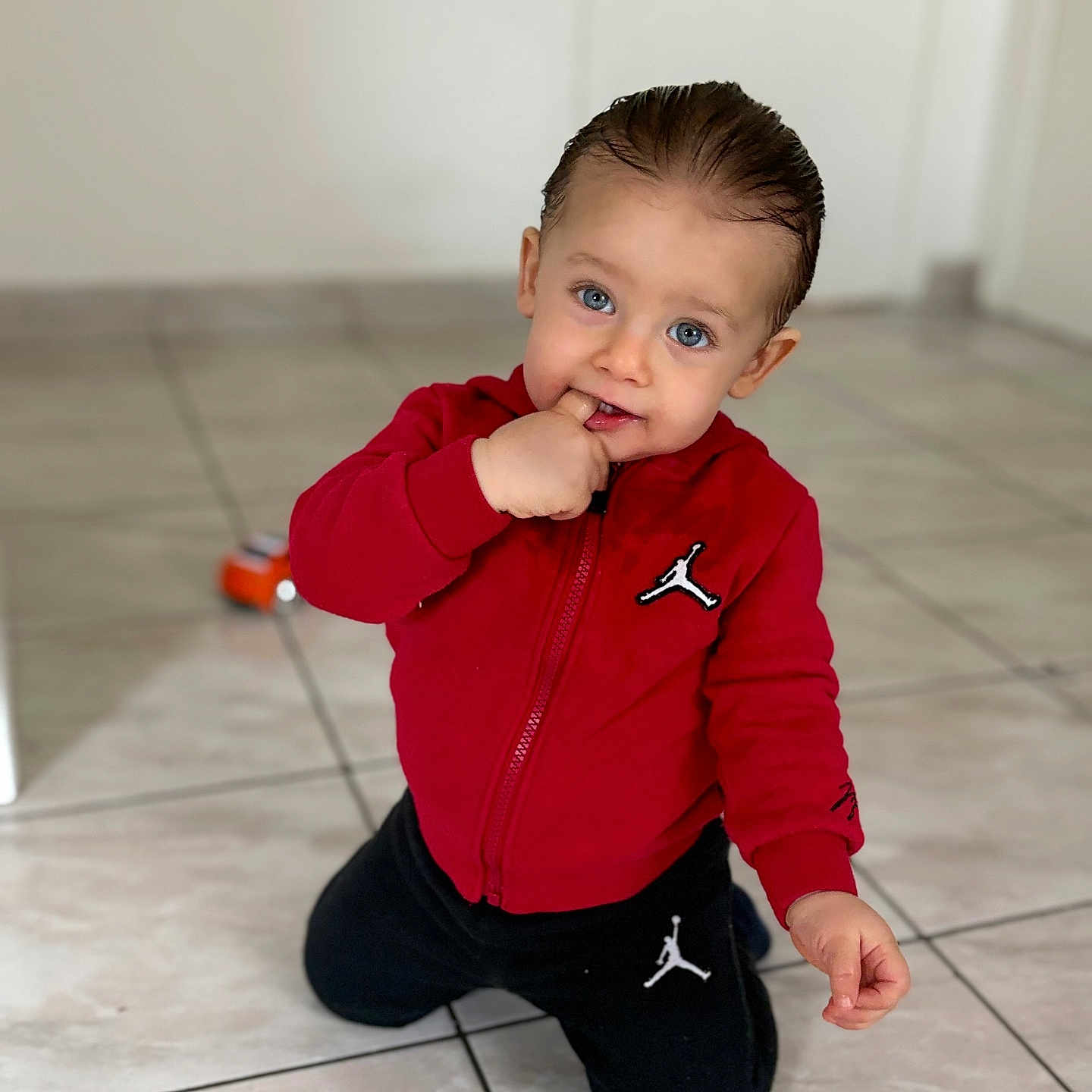 Abdelghani participe au concours pour gagner de l'argent avec cette photo : black_pants, blue_eyes, casual_clothing, child, childhood, curly_hair, cute, finger_in_mouth, floor, home, indoor, kneeling, person, playtime, portrait, red_jacket, tile_floor, toddler, toy, young_child