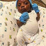 Kyson is registered to the contest to win money with this photo: baby, infant, blue_mittens, blue_hat, white_onesie, white_pants, blanket, patterned_blanket, cute, portrait, indoors, child, newborn, clothing, sleepwear, pouty_face, small_hands, sitting, soft_lighting, cozy
