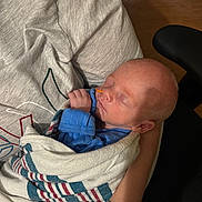 James is registered to the contest to win money with this photo: newborn, baby, sleeping, blanket, swaddled, arms, tattoo, blue_clothing, indoor, person, infant, peaceful, closeup, portrait, sleep, hand, comfort, rest, soft_light, human