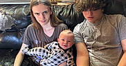 James is registered to the contest to win money with this photo: baby, child, teenager, couch, leather, siblings, smile, earbuds, long_hair, curly_hair, plaid_pajamas, indoor, window, air_conditioner, casual_clothing, family, relaxed, portrait, seated, wood_paneling