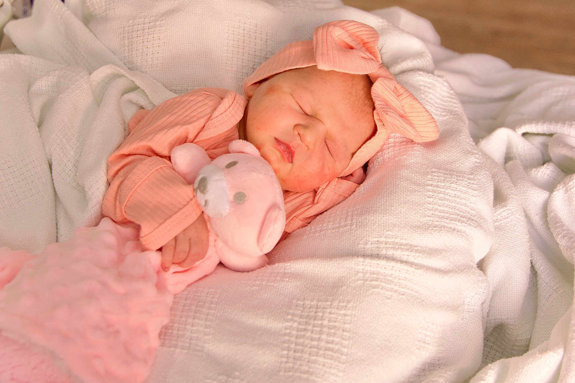 Amara is registered to the contest to win money with this photo: newborn_baby, infant, sleeping, swaddled, pink_hat, bow, plush_toy, teddy_bear, blanket, bedding, cozy, portrait, soft_texture, hand, lips, cheeks, peaceful, cute, clothing, nursery