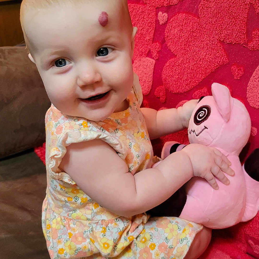 Ruby joined the competition — help win amazing prizes! baby, blue_eyes, child, couch, cozy, cute, floral_dress, happy, heart_pattern, home, indoor, infant, pink_blanket, playful, plush_toy, portrait, seated, short_hair, smiling, toy