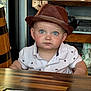 blue_eyes, brown_hat, casual_clothing, child, closeup, curious_expression, cute, face, furniture, hat, indoor, menu, person, portrait, restaurant, sitting, table, toddler, white_polo_shirt, wooden_table