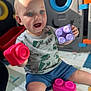 background, blonde_hair, blue_eyes, building_block, child, colorful, daylight, floor, hand, happy, indoors, plastic_toy, play_mat, playtime, shorts, sitting, smiling, toddler, toy, tshirt