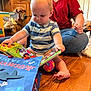 adult, baby, book, casual_clothing, child, colorful, dog, family, floor, golden_retriever, happy, home, indoor, pet, reading, sitting, smiling, striped_shirt, toy, wood
