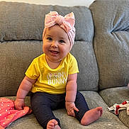 Hazel is registered to the contest to win money with this photo: baby, child, smiling, sitting, headband, bow, yellow_shirt, barefoot, couch, gray_couch, blanket, pink_blanket, polka_dot, indoor, happy, cute, infant, clothing, person, portrait