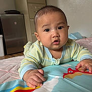 Theodore joined the competition — help win amazing prizes! baby, child, infant, pajamas, play_mat, indoor, floor, curious, hands, face, expression, person, furniture, cabinet, blanket, colorful, toy, wooden_floor, room, portrait