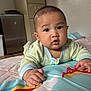 baby, child, infant, pajamas, play_mat, indoor, floor, curious, hands, face, expression, person, furniture, cabinet, blanket, colorful, toy, wooden_floor, room, portrait