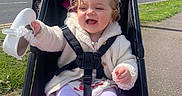 Lily is registered to the contest to win money with this photo: baby, child, daytime, greenery, happy, jacket, outdoor, person, playful, road, seatbelt, shoe, sidewalk, smile, stroller, sunny, tights, toddler, trees, urban