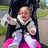 toddler, stroller, shoe, smile, child, outdoor, sunny, jacket, tights, happy, sidewalk, greenery, road, trees, daytime, baby, playful, person, seatbelt, urban