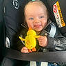 baby, child, car_seat, toy, duck, blue_bow, leather_jacket, smiling, tongue_out, cute, infant, seatbelt, clothing, person, indoor, closeup, happy, playful, hair_tie, young