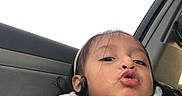 Mariana is registered to the contest to win money with this photo: child, toddler, girl, portrait, selfie, car, car_interior, seated, face, eyes, hair, scarf, white_clothing, kissy_face, funny_expression, daylight, window, close_up, casual_photo, person