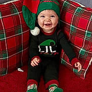 Harper joined the competition — help win amazing prizes! baby, infant, child, smiling, elf_hat, christmas, holiday, plaid, pillow, socks, red_carpet, cozy, festive, portrait, seated, smile, cute, hat, clothing, indoors