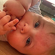 Maisy joined the competition — help win amazing prizes! baby, close_up, face, blue_eyes, hand, fingers, skin, hair, indoor, floor, wooden_floor, infant, cute, child, portrait, lying_down, person, young_child, curious, soft_lighting