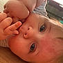 baby, close_up, face, blue_eyes, hand, fingers, skin, hair, indoor, floor, wooden_floor, infant, cute, child, portrait, lying_down, person, young_child, curious, soft_lighting