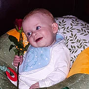 Ruairi joined the competition — help win amazing prizes! baby, child, rose, flower, bib, white_clothing, cushion, green_cushion, yellow_cushion, red_rose, smile, face, hand, indoor, portrait, cute, sitting, soft_toys, happy, young_child