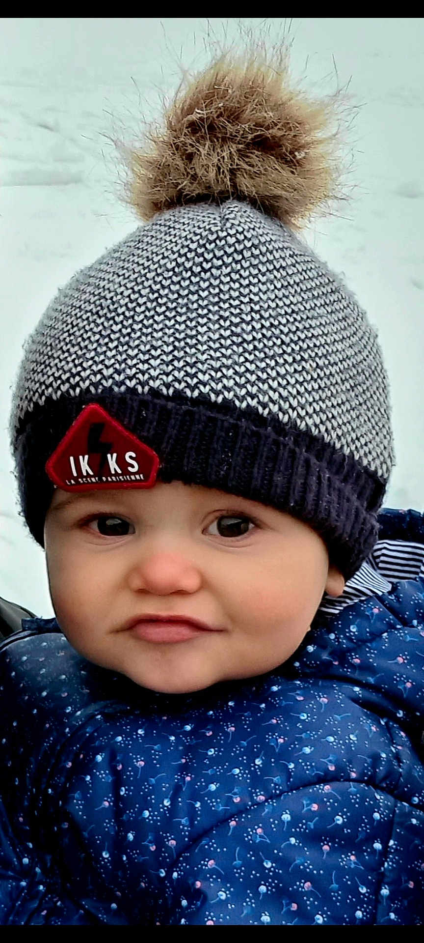 Pablo a rejoint le concours — aidez-le/la à gagner de superbes lots ! baby, child, hat, pom_pom, knitted_hat, winter_clothing, blue_jacket, rosy_cheeks, outdoor, snow, face, expression, curious, cold_weather, warm_clothing, infant, portrait, cute, closeup, person