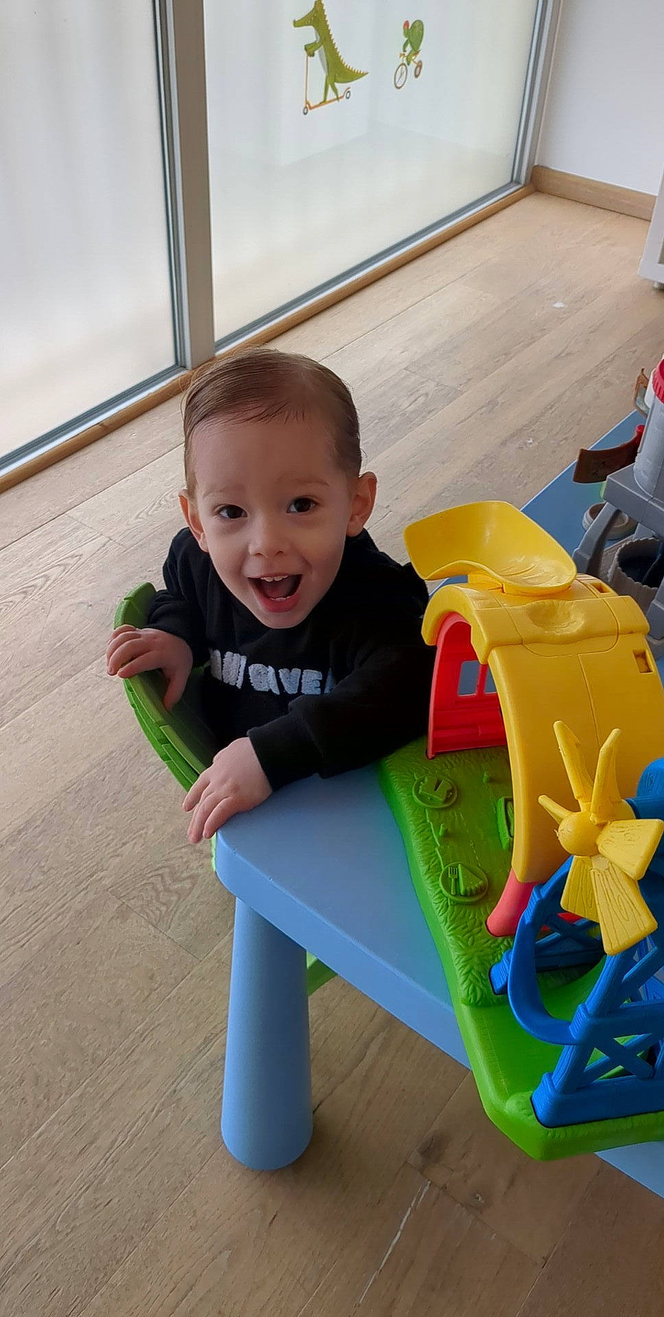 Ghjulianu participe au concours pour gagner de l'argent avec cette photo : baby, baby_playing_with_toys, baby_toddler_clothing, child, flooring, fun, leisure, person, plastic, play, recreation, room, sitting, sleeve, smile, t_shirt, table, toddler, toy, vacation