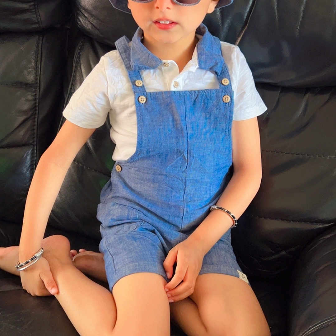 Manan is registered to the contest to win money with this photo: accessory, black_couch, blue_hat, blue_overalls, boy, bracelet, casual, child, cross_legged, cute, fashion, indoor, leather_furniture, person, portrait, relaxed, sitting, sunglasses, white_shirt, young