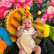 Avery joined the competition — help win amazing prizes! baby, child, costume, bee, antennae, wings, smiling, happy, sitting, flowers, roses, pink, green, plush, cushions, fabric, clothing, cute, indoor, portrait