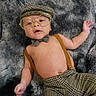 baby, infant, glasses, hat, bow_tie, suspenders, pants, plaid, pattern, blanket, fur_texture, lying_down, cute, fashion, portrait, child, face, hand, indoor, cozy