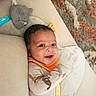 baby, infant, smile, face, clothing, bib, hat, knitted, pattern, animal_print, blanket, carpet, soft_surface, lying_down, cute, comfort, indoor, person, child, young
