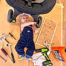 baby, tools, stroller, wrench, carpenter, work, floor, cardboard, shoe, overalls, sign, hand_tool, power_drill, pliers, hammer, toddler, screwdriver, cloth, toy, headband