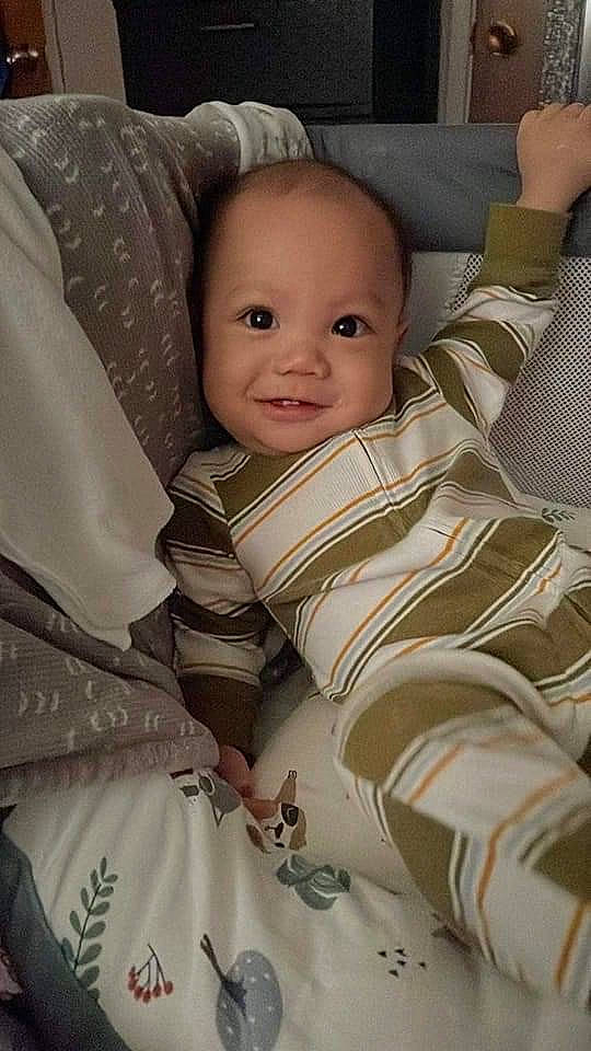 Santino is registered to the contest to win money with this photo: baby, baby_products, baby_safety, baby_toddler_clothing, bedding, cheek, child, comfort, eyebrow, happy, head, iris, linens, person, sitting, skin, sleeve, smile, textile, throw_pillow