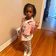 Aria is registered to the contest to win money with this photo: blackhair, child, clothing, coat, curlyhair, female, footwear, girl, hair, hardwood, head, person, shoe, sitting, sleeve, stainedwood, standing, student, wood