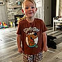 boy, casual, child, cute, dog, floor, furniture, happy, home, indoor, living_room, person, pet, plaid, scooby_doo, shorts, smiling, toy, tshirt, wood_floor