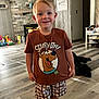 boy, casual_clothing, child, cute, dog, fireplace, floor, happy, home_decor, indoors, living_room, person, portrait, shorts, smiling, standing, stone_wall, toys, tshirt, wooden_floor
