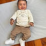 Elohïm a rejoint le concours — aidez-le/la à gagner de superbes lots ! baby, child, smiling, curly_hair, white_shoes, beige_pants, cream_shirt, teddy_bear_print, soft_mat, wooden_floor, indoor, happy, lying_down, cute, casual_clothing, footwear, infant, person, playtime, bright