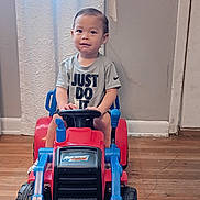 Nelson is registered to the contest to win money with this photo: toddler, child, toy, bulldozer, indoor, floor, shirt, text, face, person, vehicle, plastic, hand, expression, window, curtain, wall, door, flooring, play