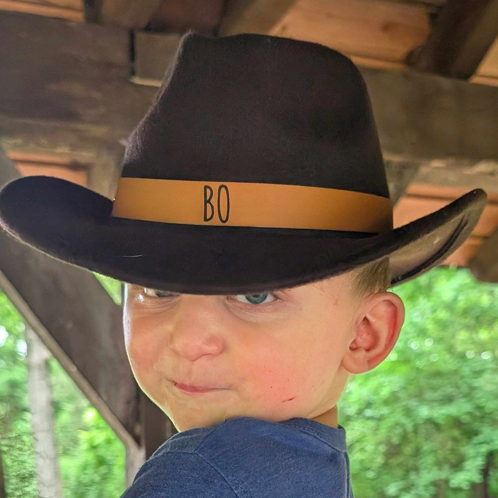 Bo Ryder is registered to the contest to win money with this photo: blue_eyes, boy, casual, child, clothing, cowboy_hat, expression, face, greenery, hat, headwear, nature, outdoor, person, portrait, profile, shelter, smirk, wood, young