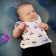 Ellie participe au concours pour gagner de l'argent avec cette photo : baby, infant, face, cherry_pattern, white_top, black_bottoms, pacifier, hand, skin, head, expression, lying_down, soft_surface, clothing, cute, child, portrait, young, relaxed, indoors