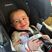 Gianni is registered to the contest to win money with this photo: baby, car_seat, infant, smile, dinosaur_print, onesie, child, seatbelt, safety, happy, cute, indoors, child_seat, person, young_child, face, hand, clothing, car, seat