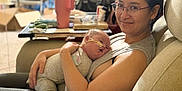 Ezekiel joined the competition — help win amazing prizes! woman, baby, glasses, feeding_tube, couch, living_room, smile, holding, relaxing, clothing, person, infant, medical_device, home, comfort, seated, casual, care, parent, indoor
