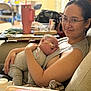 woman, baby, glasses, feeding_tube, couch, living_room, smile, holding, relaxing, clothing, person, infant, medical_device, home, comfort, seated, casual, care, parent, indoor