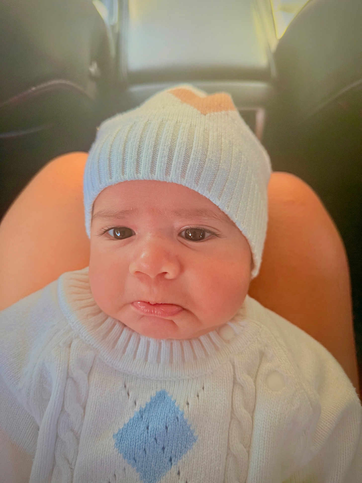 Athan joined the competition — help win amazing prizes! baby, infant, face, pout, knit_hat, sweater, clothing, person, child, indoors, car, seat, lap, cute, expression, portrait, headwear, warm_clothing, skin, young