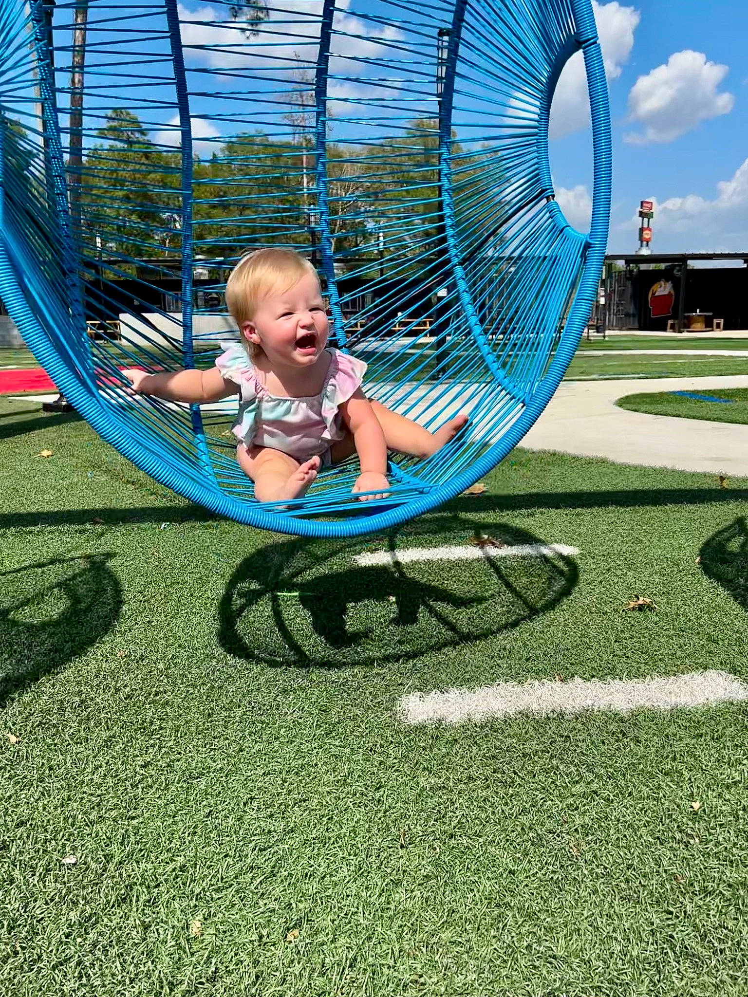 Harper is registered to the contest to win money with this photo: baby, circle, city, cloud, electric_blue, fun, grass, leisure, nonbuilding_structure, outdoor_play_equipment, person, plant, playground, recreation, shade, sky, smile, symmetry, toddler, tree