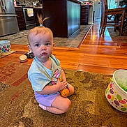 Chloe is registered to the contest to win money with this photo: bucket, cabinet, carpet, child, curious, floor, hair_tie, home, indoor, kitchen, person, play, refrigerator, shorts, sitting, stove, toddler, toy, tshirt, wooden_floor
